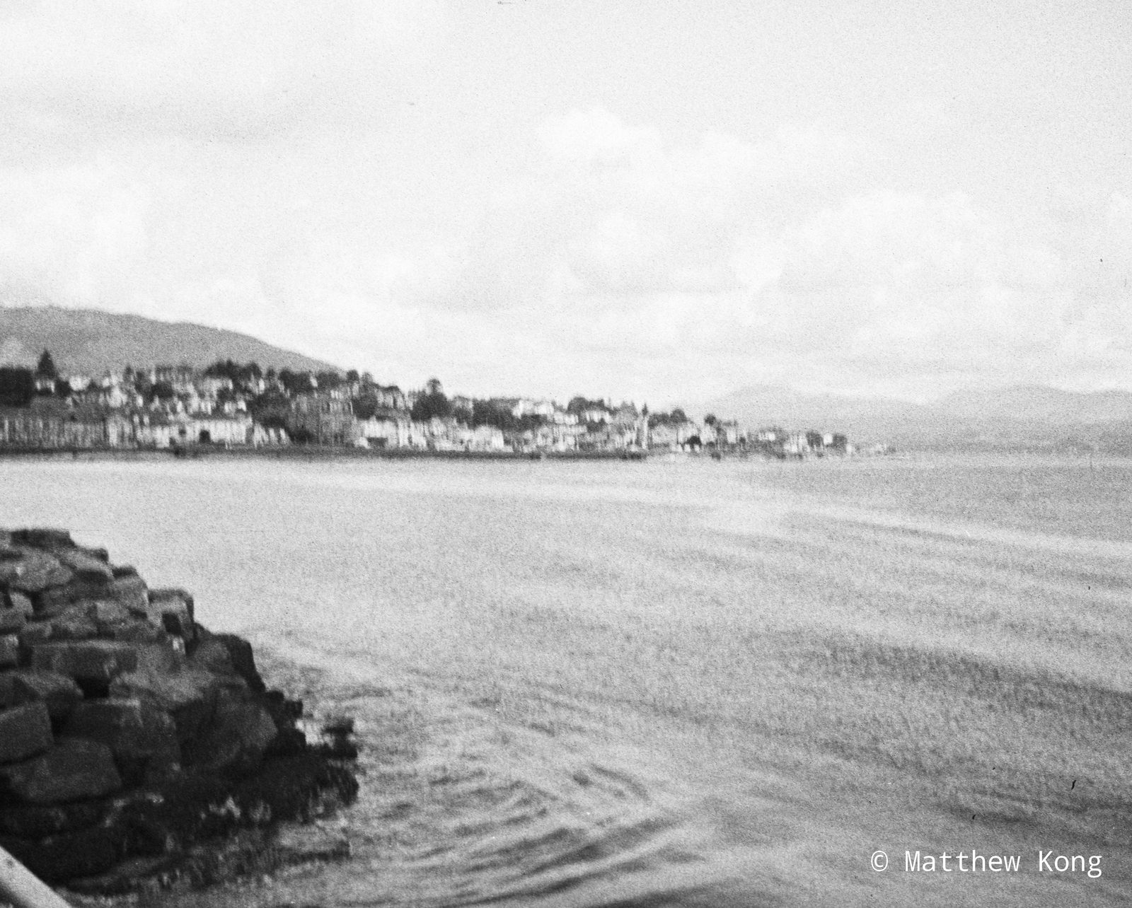 The town seen from the rocks across the water, its terraces stacked along the shore under the hills.
